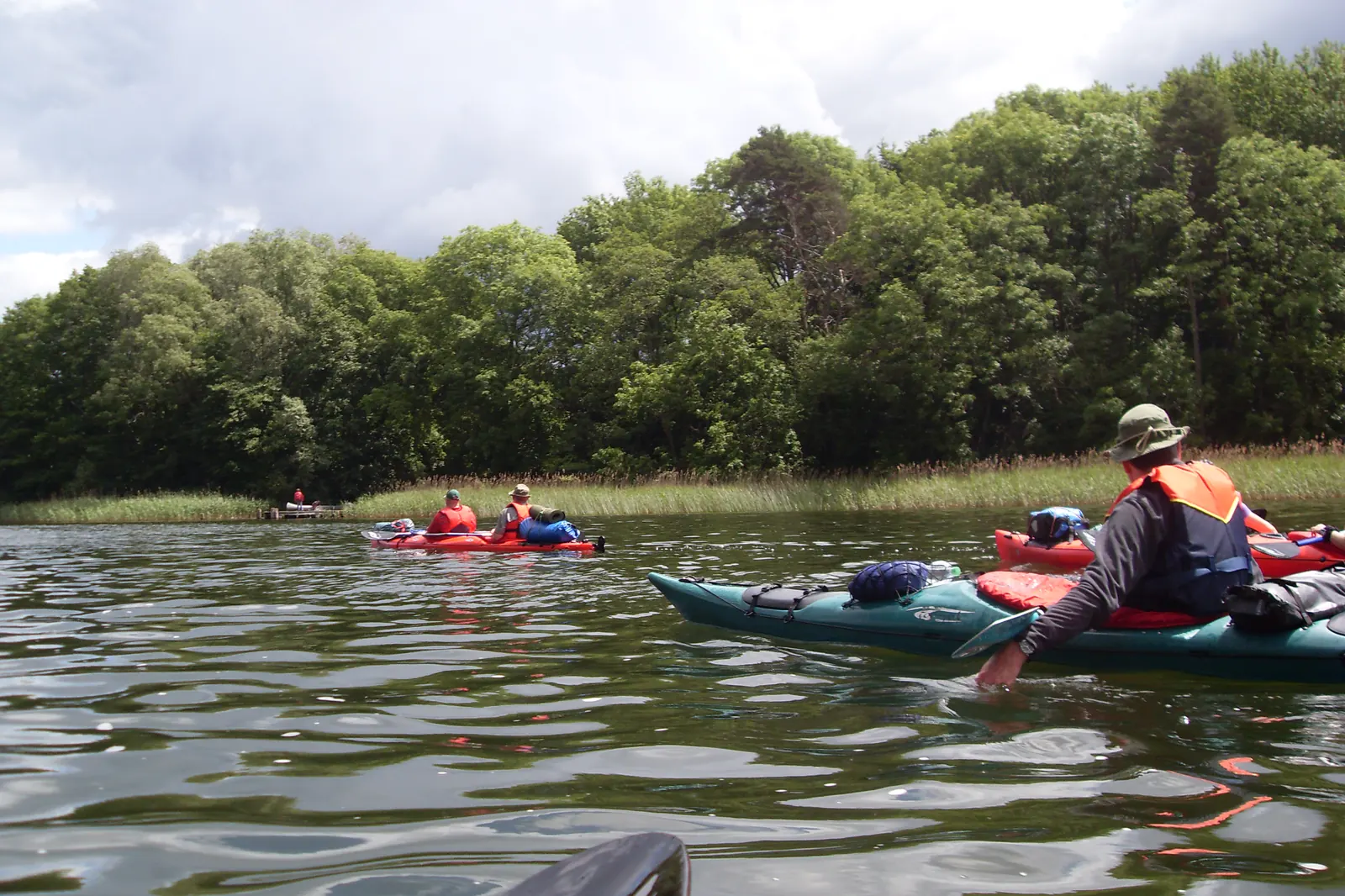 Faltboote und Kajaks mit Gepäck auf dem Canower See, am Ufer Schilf und Laubwald